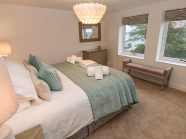 A bedroom with a bed covered in green bedding and pillows next to a dresser and two windows with a bench below them at Fal View in Falmouth
