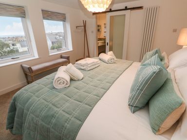 A bedroom with a bed covered with green bedding and rolled towels near two windows and a bench at Fal View in Falmouth
