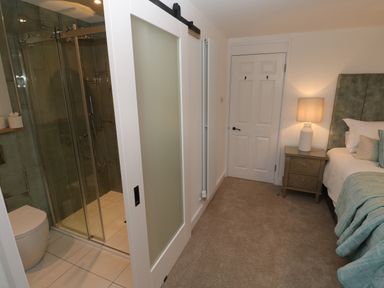 A bedroom with a nightstand and lamp next to a bed and a bathroom with a sliding door at Fal View in Falmouth