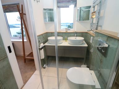A bathroom with twin sinks a toilet a glass shower door and a window with a view at Fal View in Falmouth