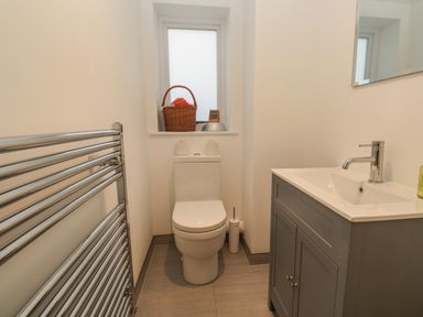 A bathroom with a toilet, sink with cabinet, heated towel rack, and a window with a basket on the sill at Fal View in Falmouth