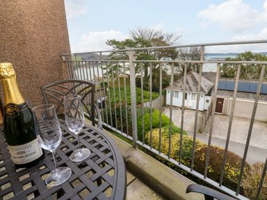 A balcony with a metal table holding a bottle of champagne and two glasses overlooking nearby houses and trees at Fal View in Falmouth