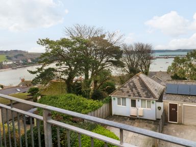 A view of a small house with a sloped roof next to a garage overlooking a river with boats and hills in the background at Fal View in Falmouth