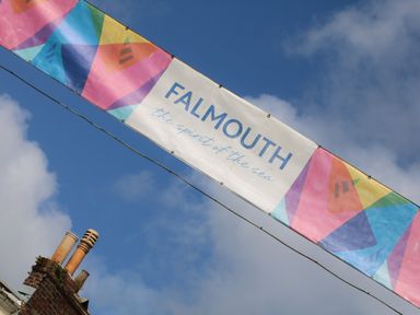 A banner with colorful geometric shapes and the word Falmouth hanging above a building with chimneys against a blue sky at Fal View in Falmouth