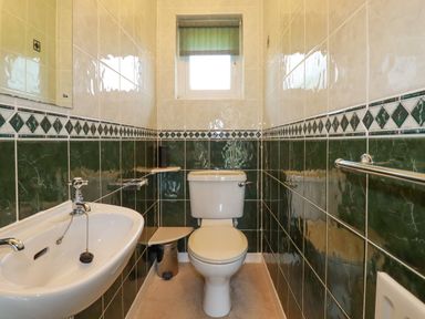 A small bathroom with a toilet sink green and beige tiled walls and a small window at Trestar in Polzeath