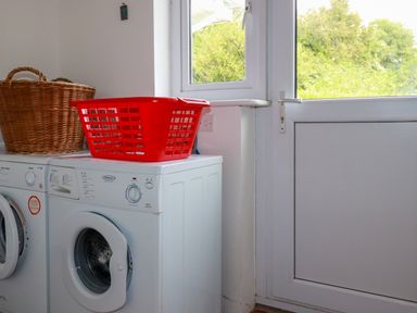 A laundry room with a washing machine and dryer with baskets on top next to a door with windows at Trestar in Polzeath