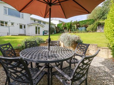 A patio with a round metal table and five chairs under an umbrella in a garden at Trestar in Polzeath
