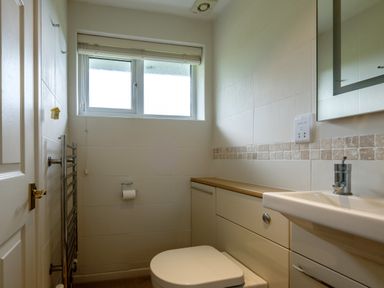 A small bathroom with a toilet sink cabinet and a frosted window at Trestar in Polzeath