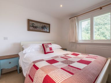A bedroom with a bed covered in a red and white patchwork quilt and a pillow next to a window with white curtains at Trestar in Polzeath