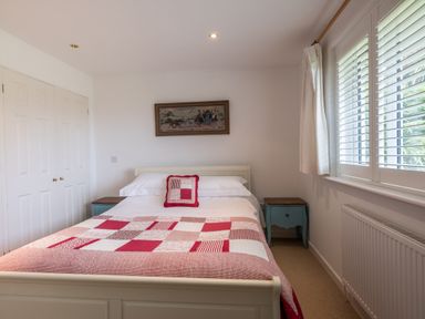 A bedroom with a double bed with a red and white patchwork quilt and two blue bedside tables at Trestar in Polzeath