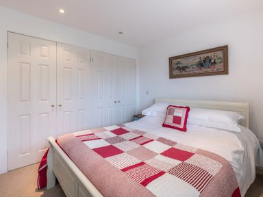 A bedroom with a double bed covered with a red and white patchwork quilt and a small pillow on the bed a framed artwork on the wall and built-in wardrobes with white doors at Trestar in Polzeath
