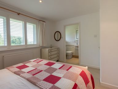 A bedroom with a bed covered with a red and white checkered blanket a chest of drawers a round mirror and an en suite bathroom at Trestar in Polzeath
