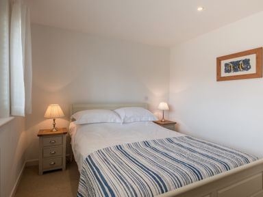A bedroom with a double bed with striped blanket and two bedside tables with lamps at Trestar in Polzeath