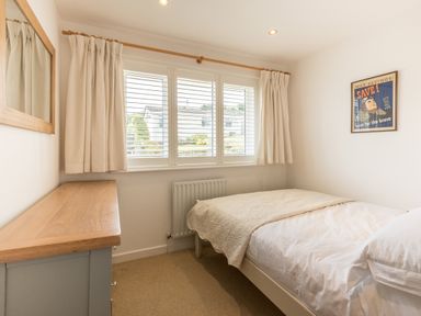 A bedroom with a single bed a chest of drawers a window with curtains and a framed picture on the wall at Trestar in Polzeath