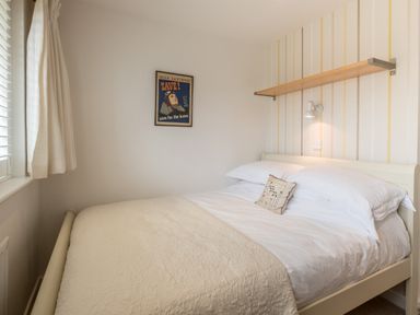 A bedroom with a double bed, a framed wall poster, a wooden shelf, a wall light, and a window with curtains at Trestar in Polzeath