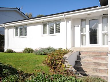 The exterior of a white building with windows and a glass door with concrete stairs and garden at Trestar in Polzeath