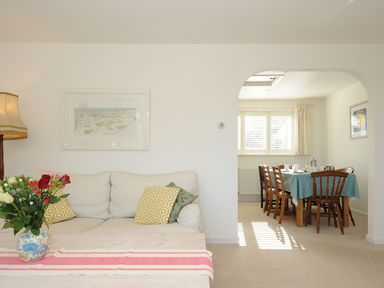 A living room with a sofa and cushions and a coffee table with flowers next to a dining room with a table and chairs at Trestar in Polzeath