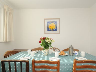 A dining table with a polka dot tablecloth set with cups plates a vase of flowers croissants and a coffee pot at Trestar Polzeath