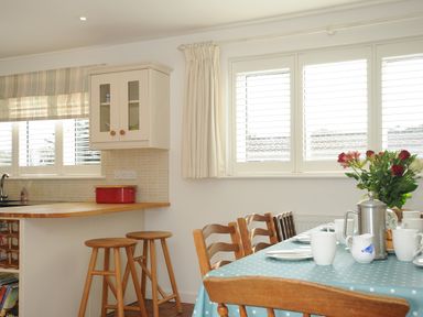 A kitchen area with bar stools and a dining table set with cups and plates at Trestar in Polzeath