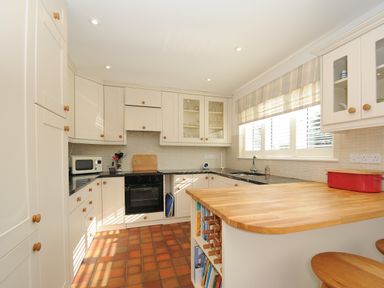 A kitchen with white cabinets black countertops and a wooden island with shelves and stools at Trestar Polzeath