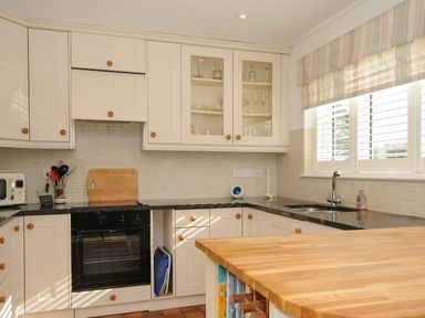 A kitchen with white cabinets black countertop a wooden island and a window with blinds at Trestar in Polzeath