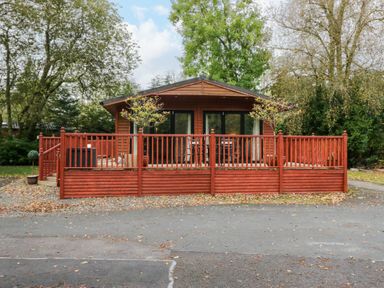 A wooden cabin with a red painted deck and railings surrounded by trees at Somerford Lodge Langdale 7 White Cross Bay near Windermere