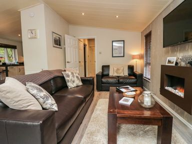 A living room with dark leather sofas a wooden coffee table a wall-mounted electric fireplace and a television at Somerford Lodge Langdale 7 White Cross Bay near Windermere