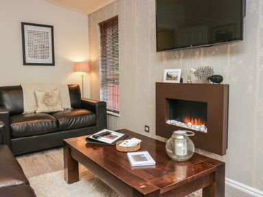 A living room with brown leather sofas a wooden coffee table a wall-mounted electric fireplace and a flat screen TV at Somerford Lodge Langdale 7 White Cross Bay near Windermere