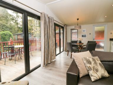 A living room with a sofa and pillows next to sliding glass doors leading to a deck and a dining table with chairs at Somerford Lodge Langdale 7 White Cross Bay near Windermere