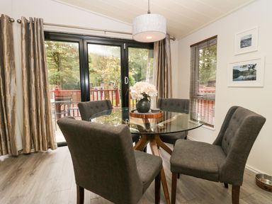 A dining area with a round glass table and four gray chairs near large sliding glass doors at Somerford Lodge Langdale 7 White Cross Bay near Windermere