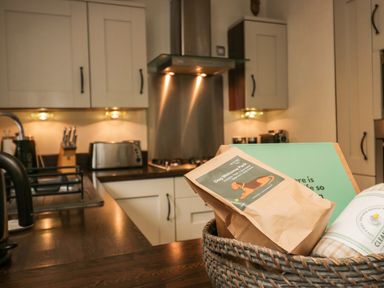 A kitchen with white cabinets wooden countertop knife block toaster and a basket with a dog welcome pack at Somerford Lodge Langdale 7 White Cross Bay near Windermere