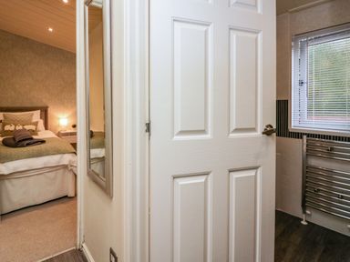 A view of a bedroom with a bed and lamp through an open door next to a bathroom with a window and towel radiator at Somerford Lodge Langdale 7 White Cross Bay near Windermere