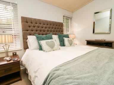 A bedroom with a brown tufted headboard white bedding green pillows and bedside tables with lamps at Somerford Lodge Langdale 7 White Cross Bay near Windermere