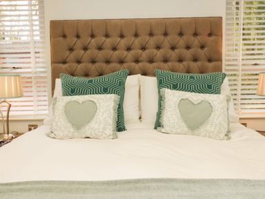 A bed with a brown tufted headboard with green and white pillows and bedside lamps at Somerford Lodge Langdale 7 White Cross Bay near Windermere