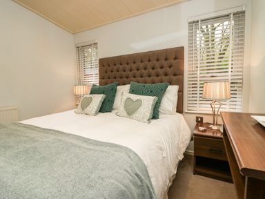 A bedroom with a bed with green and white pillows two bedside tables with lamps and windows with blinds at Somerford Lodge Langdale 7 White Cross Bay near Windermere