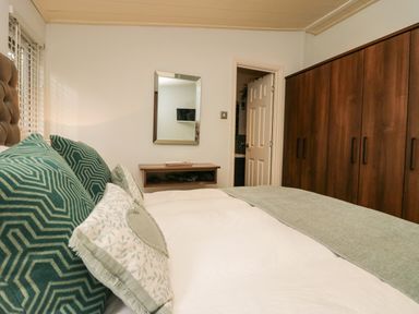 A bedroom with a bed pillows a wall-mounted mirror a dresser a door and a wooden wardrobe at Somerford Lodge Langdale 7 White Cross Bay near Windermere