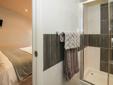 A bathroom with a towel rack holding two towels next to a shower with black and white tiles and a view into a bedroom with a bed and blanket at Somerford Lodge Langdale 7 White Cross Bay near Windermere