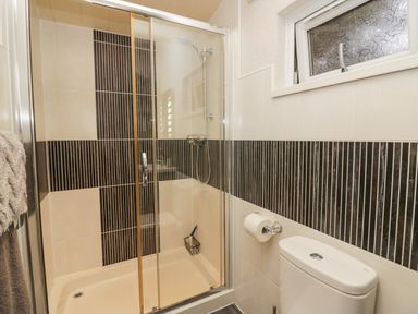 A bathroom with a shower enclosure with glass doors a toilet and a frosted window at Somerford Lodge Langdale 7 White Cross Bay near Windermere