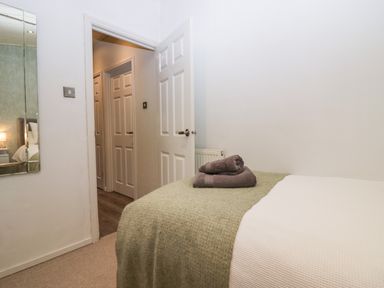 A bedroom with a bed covered with a green blanket and towels on top and an open door showing a hallway with doors