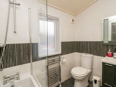 A bathroom with a shower over a bathtub a toilet a window with blinds a towel radiator and a sink cabinet at Somerford Lodge Langdale 7 White Cross Bay near Windermere