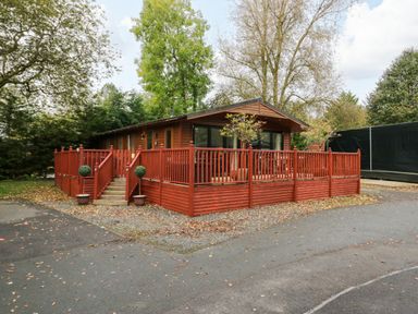 A wooden cabin with a large red deck and stairs surrounded by trees at Somerford Lodge Langdale 7 White Cross Bay near Windermere