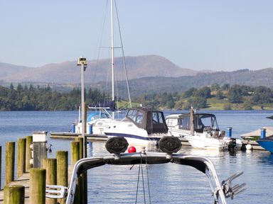 A dock with boats moored on a lake with hills and trees in the background at Somerford Lodge Langdale 7 White Cross Bay near Windermere