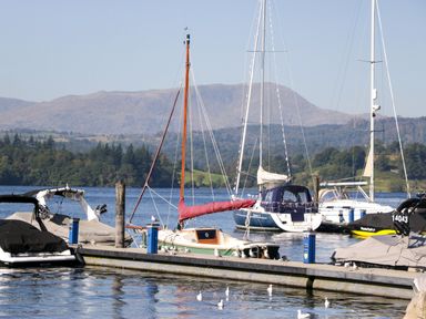 A dock with several boats moored on a lake with mountains and trees in the background at Somerford Lodge Langdale 7 White Cross Bay near Windermere