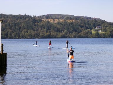 Four people paddleboarding on a lake with a forested hill in the background at Somerford Lodge Langdale 7 White Cross Bay near Windermere