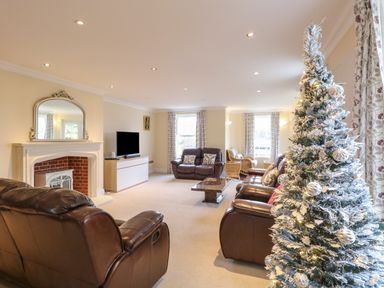 A living room with brown leather sofas a decorated Christmas tree and a fireplace at The Little House in Horning