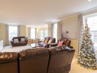 A living room with leather sofas a decorated Christmas tree and floral curtains at The Little House in Horning
