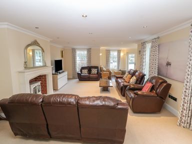 A living room with brown leather sofas a fireplace a flat screen tv and floral curtains at The Little House in Horning