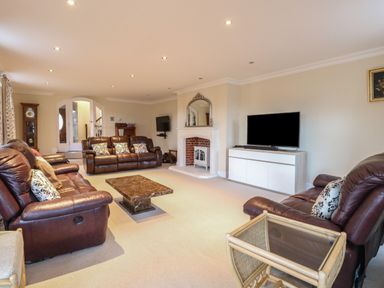 A living room with brown leather sofas a coffee table a television and a fireplace at The Little House in Horning