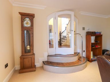 A room with a wooden grandfather clock a small wooden bookshelf two steps leading to white double doors with glass panels at The Little House in Horning