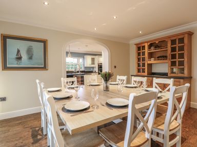A dining room with a wooden table set for eight and a wooden cabinet visible through an archway at The Little House in Horning